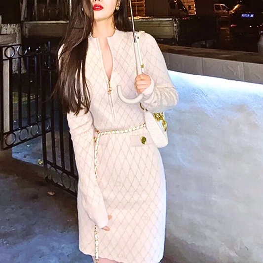 アイボリーのフロントジップニットワンピース。屋外で花束を片手に持ち正面に立つ姿。胸元のファスナーとミニ丈