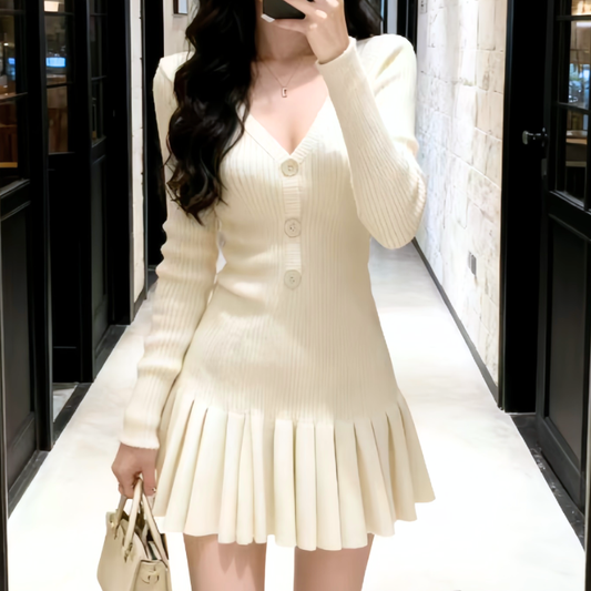 アイボリーのVネックボタン付きリブニットワンピース。女性が通路でスマートフォンを構えた正面。ウエストに沿う縦リブと広がる裾