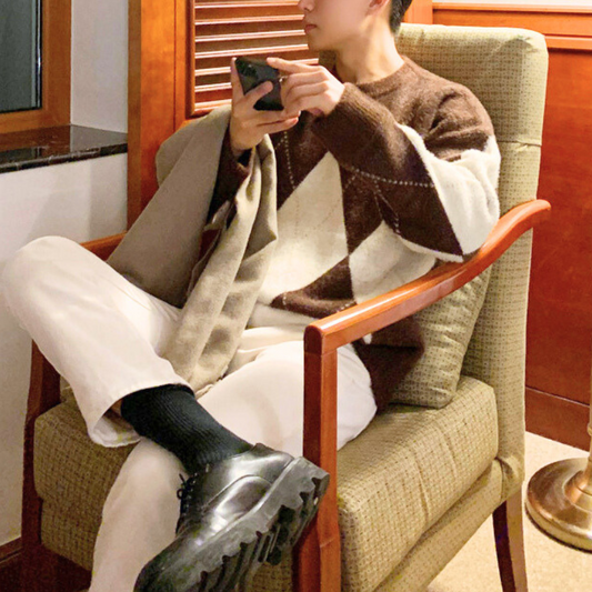 アーガイル柄ニットを着た男性が椅子に座ってスマホを操作している様子