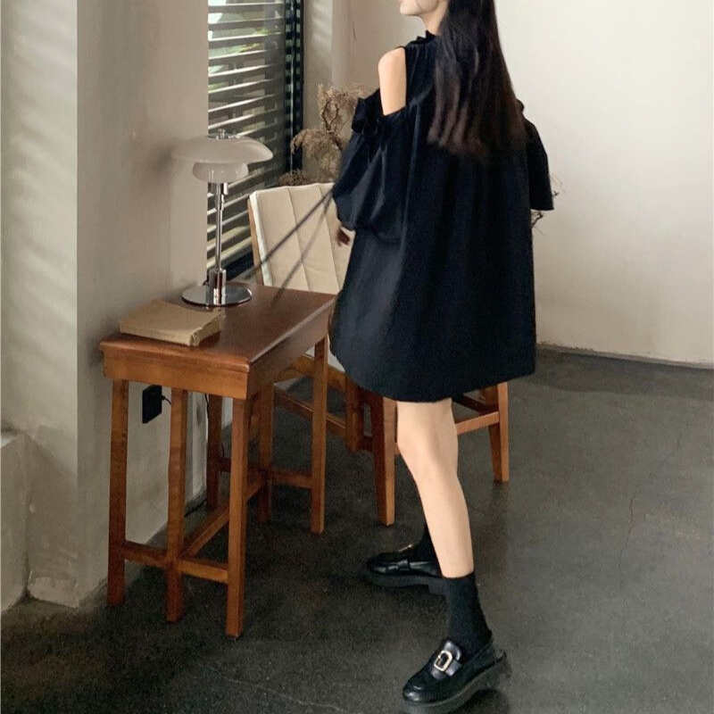 落ち着いたブラックのギャザーワンピースで椅子に座る女性。