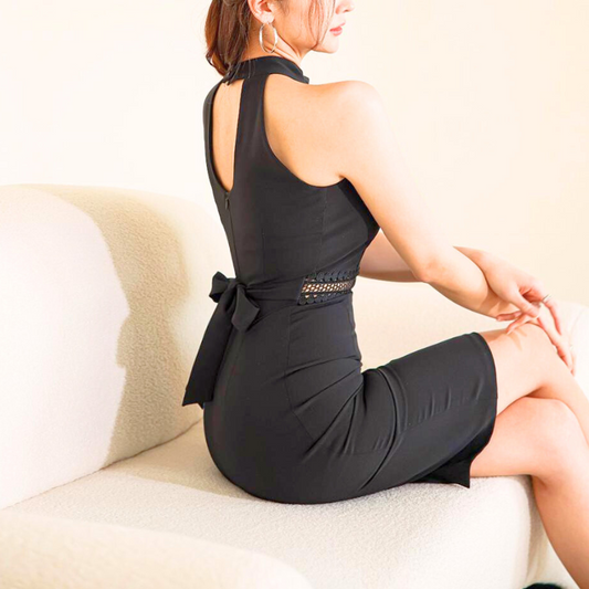 背中のリボンがアクセントの黒タイトワンピースをソファで座って着用