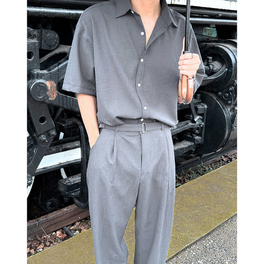 チャコールの開襟シャツセットアップを着た男性が電車前で立つ様子