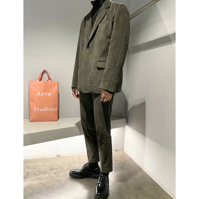 Acne Studiosの紙袋を背景に立ったカーキコーデュロイスーツ全身スタイル