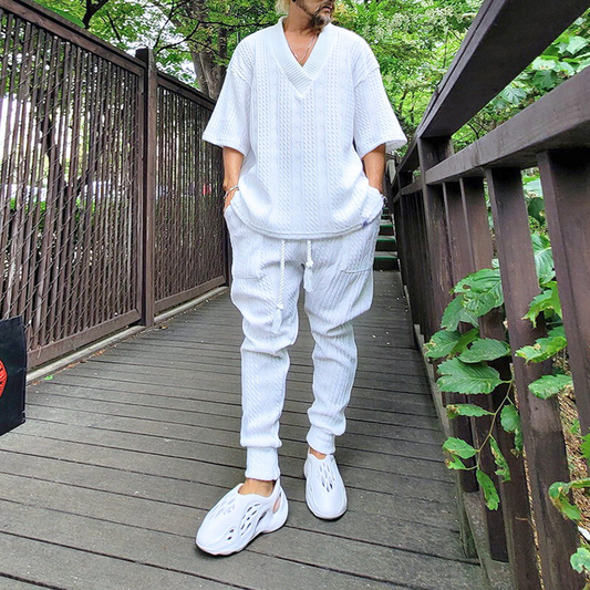 白いジャガードニットセットアップを着て橋の上を歩く男性