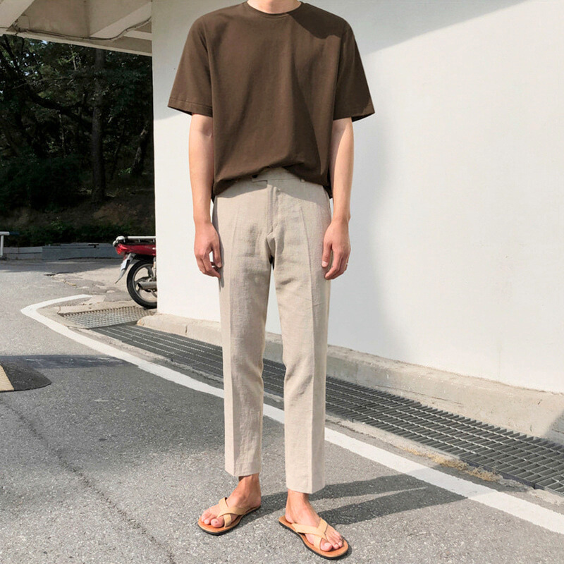 ベージュのコットンリネン素材テーパードパンツを着用した男性。シンプルなTシャツとサンダルで涼しげな夏コーデに。