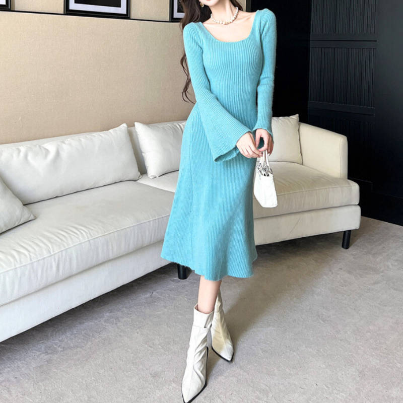 室内でブルーのフレアラインニットワンピースを着る女性