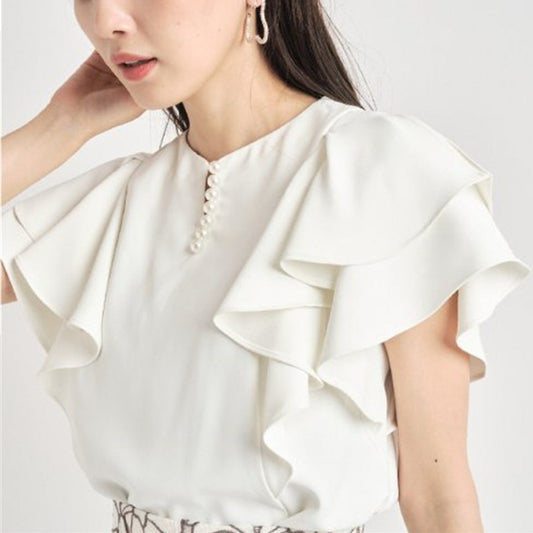 斜めから見たフリルスリーブブラウスで、肩まわりの華奢見え効果とパール装飾の上品さを強調