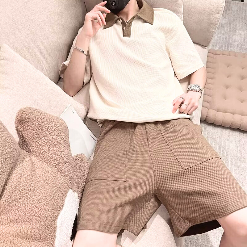 配色ポロとブラウンパンツのセットアップでソファに座る男性・夏のルームウェア提案