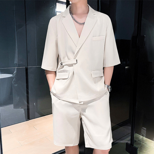 ブラックの背景に立ち、シンプルなポーズでアイボリーのセットアップを着る男性モデル