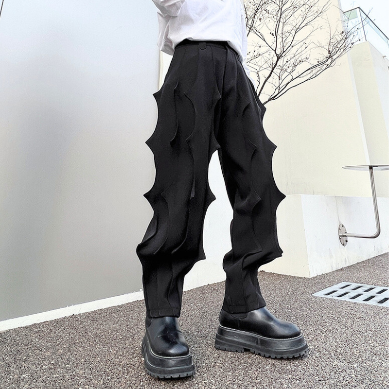 シンプルな壁前で立ちポーズする立体的デザインの黒パンツ
