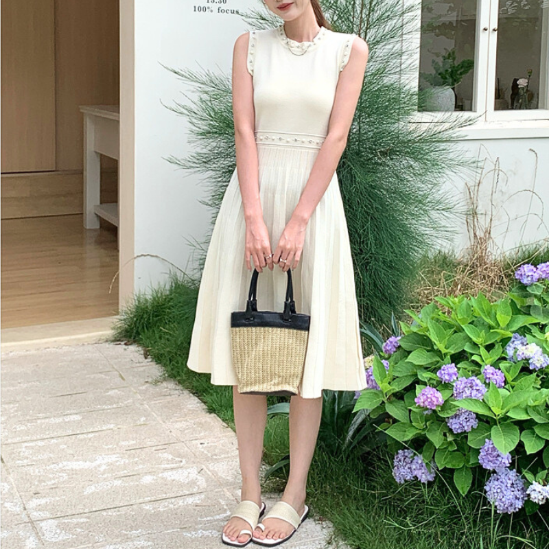 ホワイトのノースリニットワンピを草花の前で立ち姿で撮影