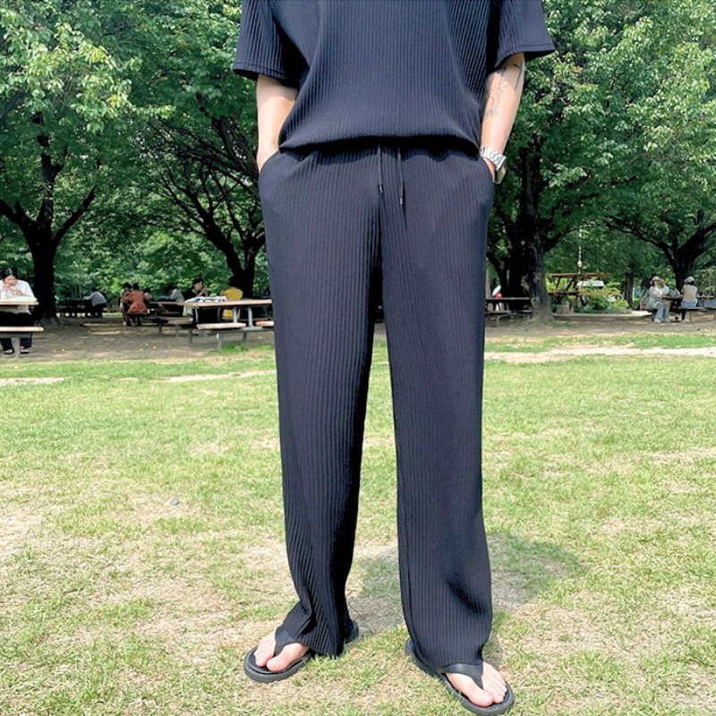 黒のプリーツセットアップで立ち止まる男性のフロント姿