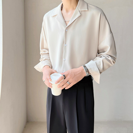 とろみ素材のベージュシャツを着た男性が正面でコーヒーを持って立つ様子