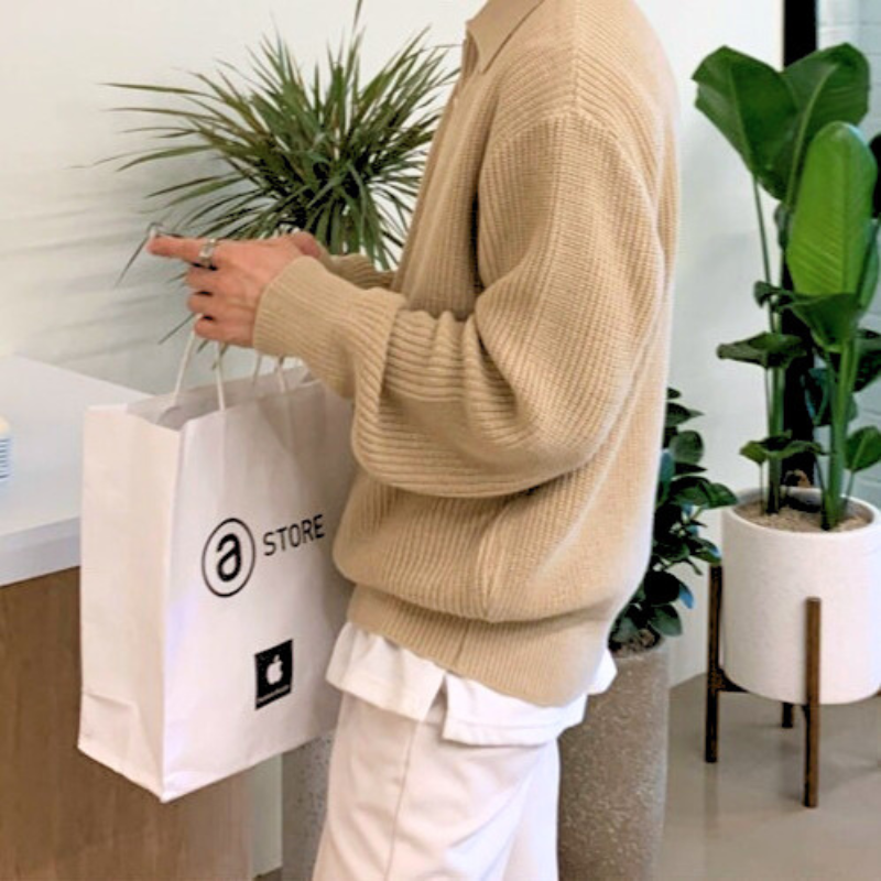 ベージュのニットを着てショッピングバッグを持つ横向きの男性