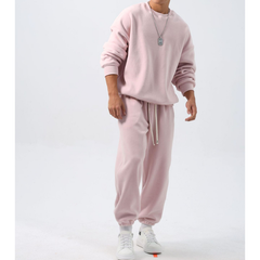 ピンクのクルーネックトップスと裾絞りワイドパンツのフリースセットアップを着た男性。袖をたくし上げ、両腕を下げて白いスニーカーを合わせた正面の全身姿