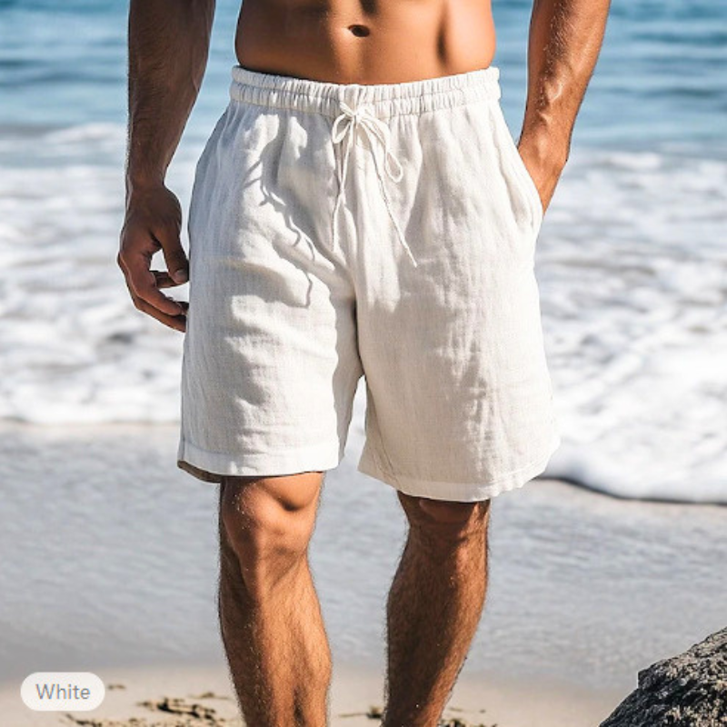 ホワイトのメンズリネン混ショートパンツを穿いた男性の海辺コーデ
