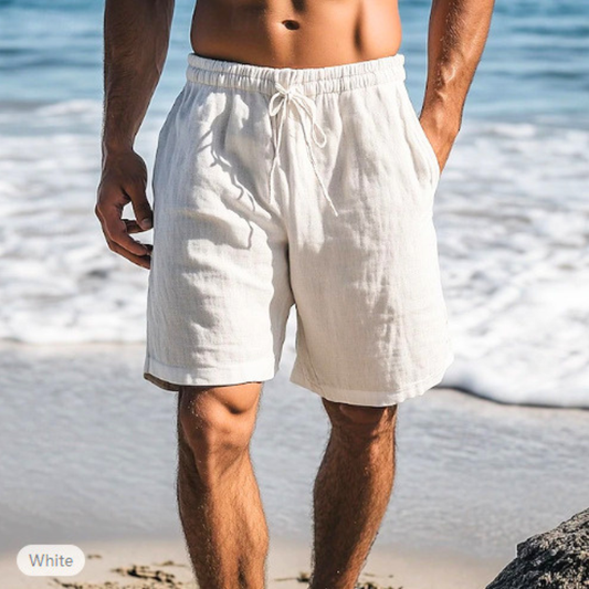 ホワイトのメンズリネン混ショートパンツを穿いた男性の海辺コーデ