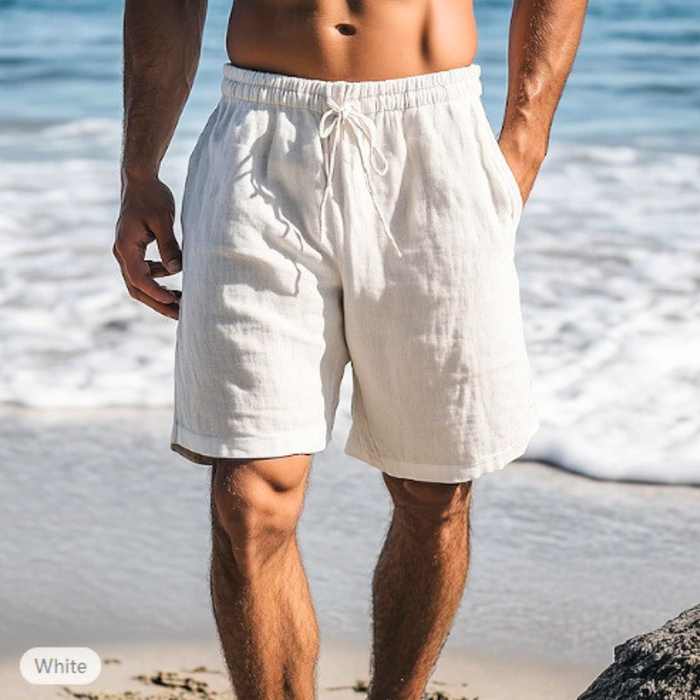 ホワイトのメンズリネン混ショートパンツを穿いた男性の海辺コーデ