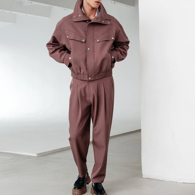 ブラウンのスタンドカラーブルゾンとハイウエストタックパンツのセットアップを着用した男性の全身正面