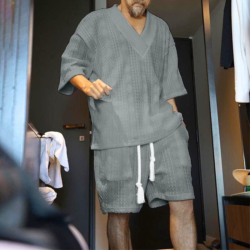 グレーの立体編みVネック半袖ニットとショートパンツセットアップを着た男性