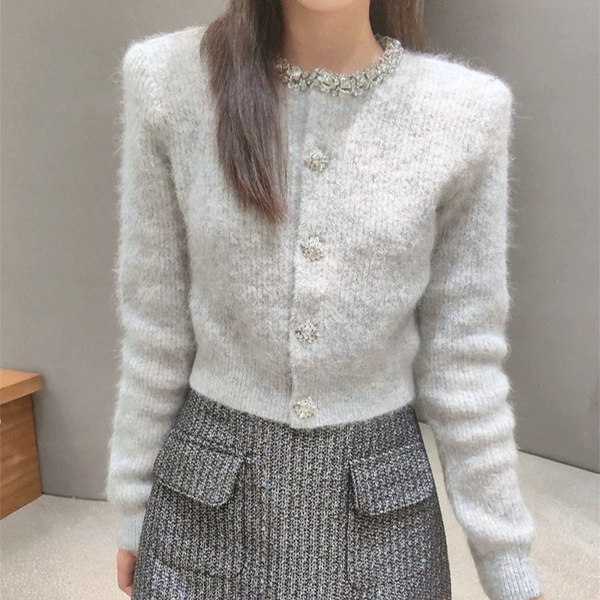グレーのネックビジュー付きショート丈ニットカーディガン。女性がグレーのカーディガンを着た正面の上半身。首元のビジューと花形ボタン、短めの裾