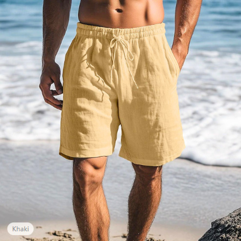 ベージュのメンズリネン混ショートパンツを穿いた男性の海辺コーデ