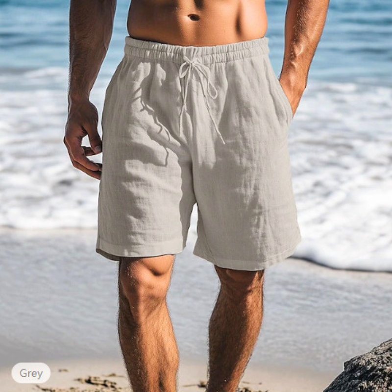 グレーのメンズリネン混ショートパンツを穿いた男性の海辺コーデ