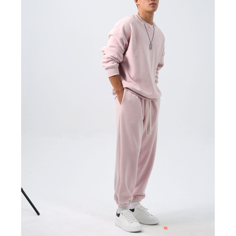 ピンクのクルーネックトップスと裾絞りワイドパンツのフリースセットアップを着た男性。両手をパンツのポケットに入れ、裾を絞ったパンツの丸みが見える斜め横の全身姿