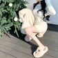 ホワイトのシャギーニットセットアップ。クリスマスツリーの横で片手を頭に添えて座る姿。ミニスカートと長袖トップス