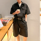 ブラックの半袖カーゴジャンプスーツを本と合わせた男性の正面コーデ