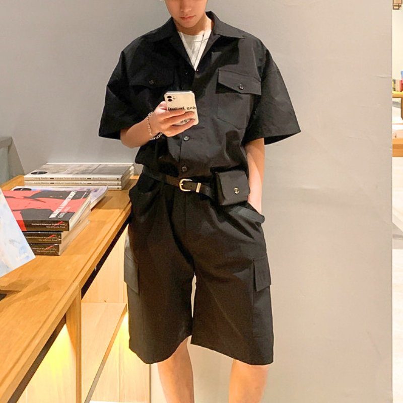 ブラックの半袖カーゴジャンプスーツを本と合わせた男性の正面コーデ
