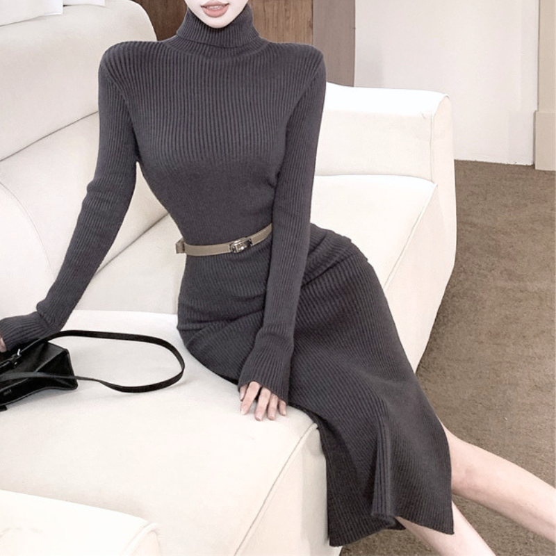 グレーのベルト付きハイネックタイトニットワンピース。女性がソファに座った正面からの着用姿。首元のリブとベルト、長いスカート部分