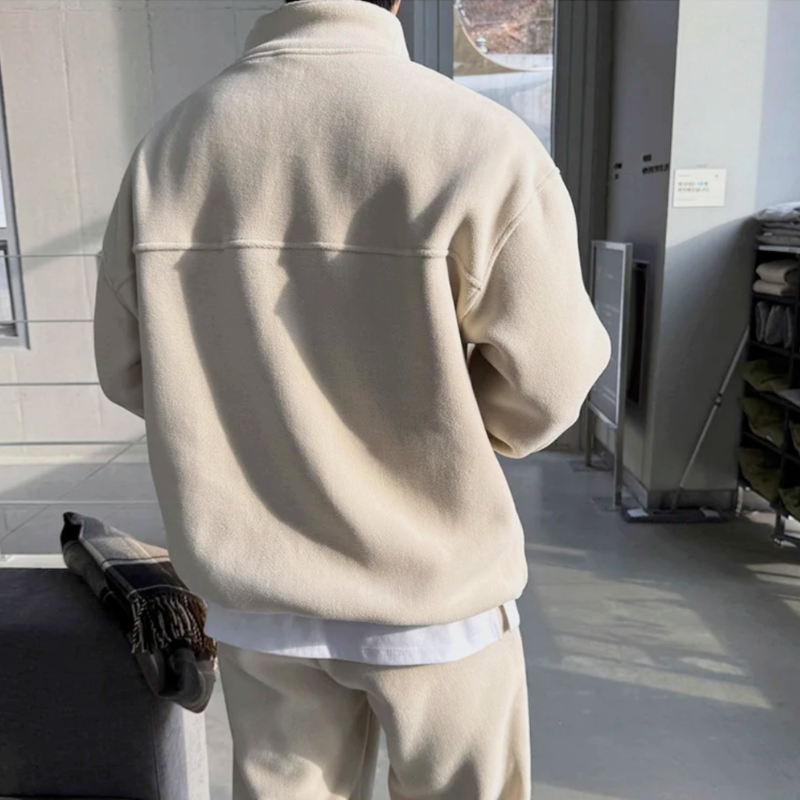 アイボリーのスタンドカラープルオーバーとワイドパンツのセットアップを着た男性。背面の横切り替えと肩を落とした袖、裾から見える白いインナーを写した後ろ姿