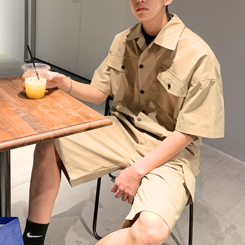 ベージュの半袖カーゴジャンプスーツをカフェで着た男性の座りコーデ