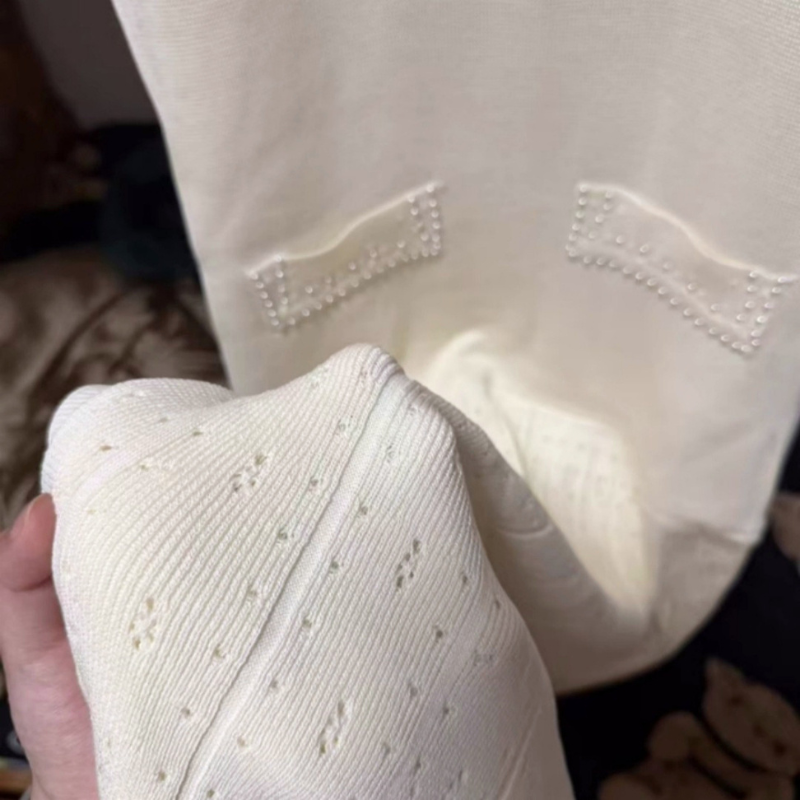 アイボリーのパール風装飾ニットワンピース。ワンピースの腰元とスカートのアップ。ポケット風の縁取りと小花の透かし模様