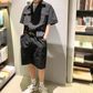 ブラックの半袖カーゴジャンプスーツを本棚の前で着た男性の立ち姿
