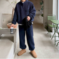 ネイビーのスタンドカラープルオーバーとワイドパンツのセットアップを着た男性。片手をカップの置かれた台へ伸ばし、もう片手で黒いマフラーを持つ全身姿