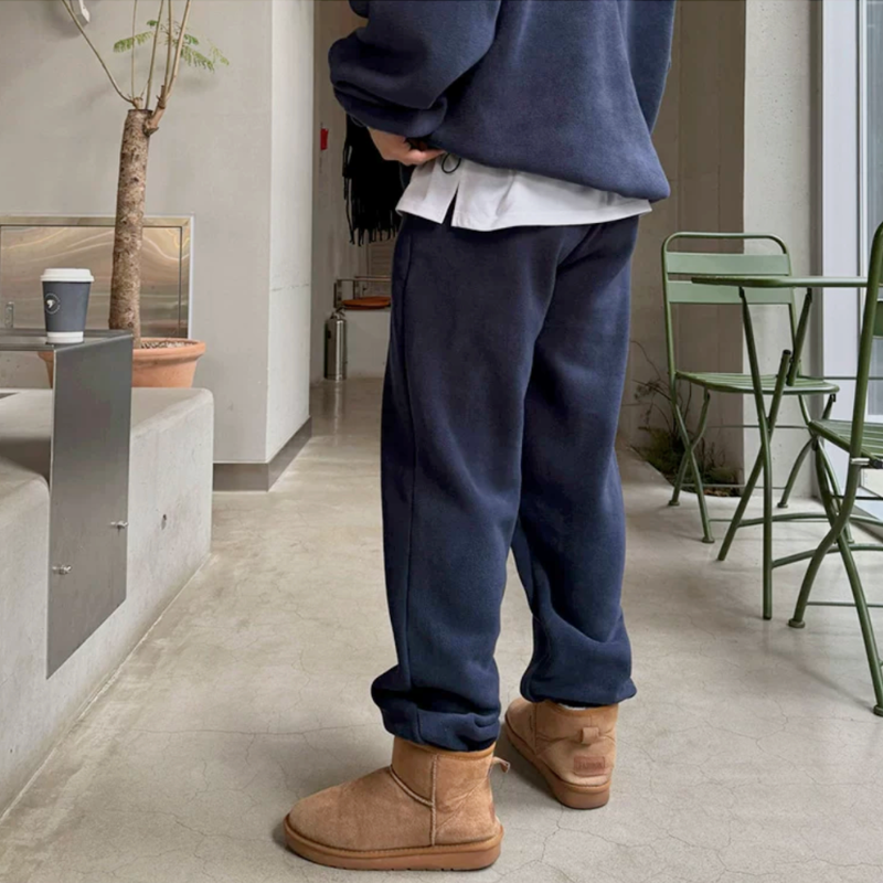 ネイビーのスタンドカラープルオーバーとワイドパンツのセットアップを着た男性。斜め後ろからパンツのゆったりしたラインとキャメル系ブーツを写した姿