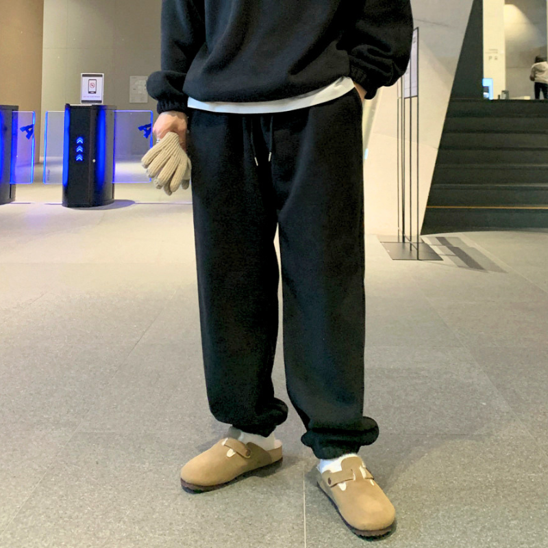 ブラックのスタンドカラープルオーバーとワイドパンツのセットアップを着た男性。片手をパンツのポケットに入れ、ゆったりしたパンツとベージュ系の靴を写した姿