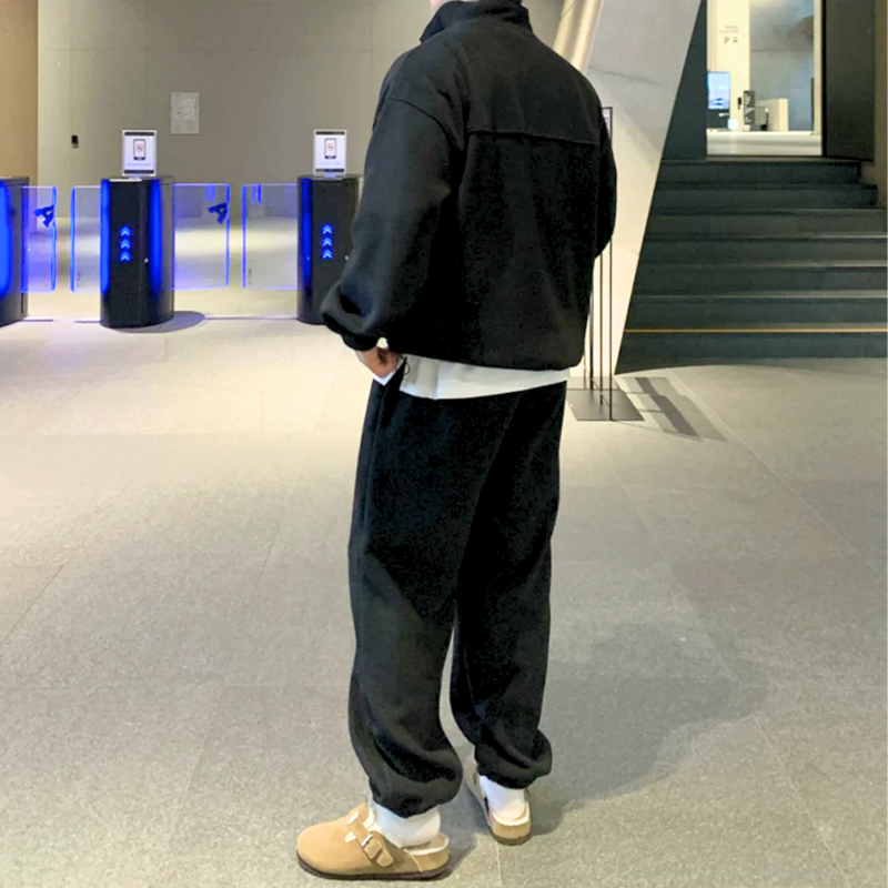 ブラックのスタンドカラープルオーバーとワイドパンツのセットアップを着た男性。片手をパンツのポケットに入れ、背中の横切り替えとパンツの後ろ姿を見せた全身姿