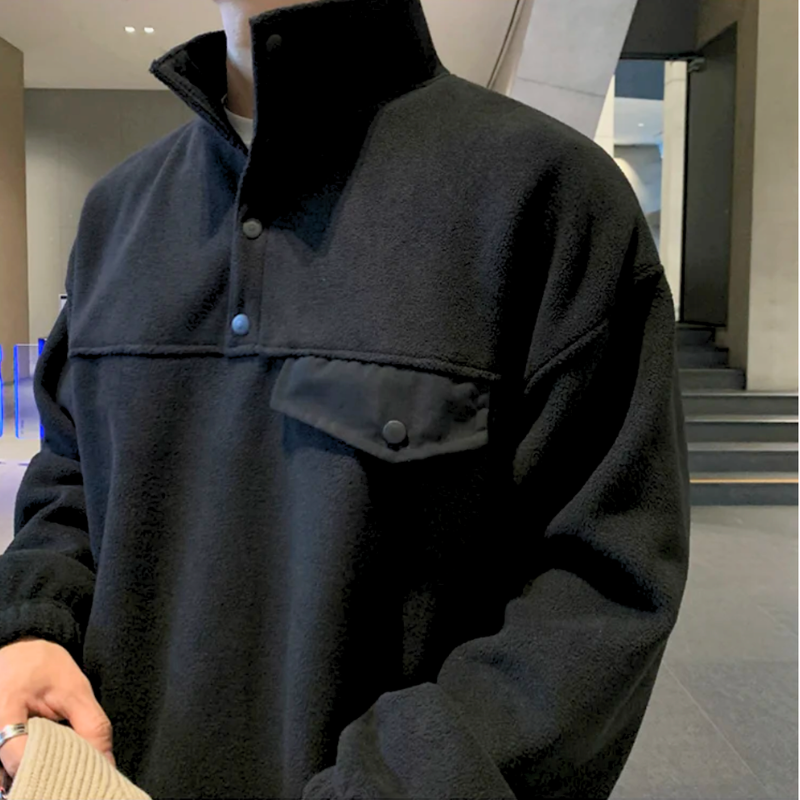 ブラックのスタンドカラープルオーバーとワイドパンツのセットアップを着た男性。立ち襟と胸の横切り替え、フラップ型ポケットを斜めから大きく写した姿