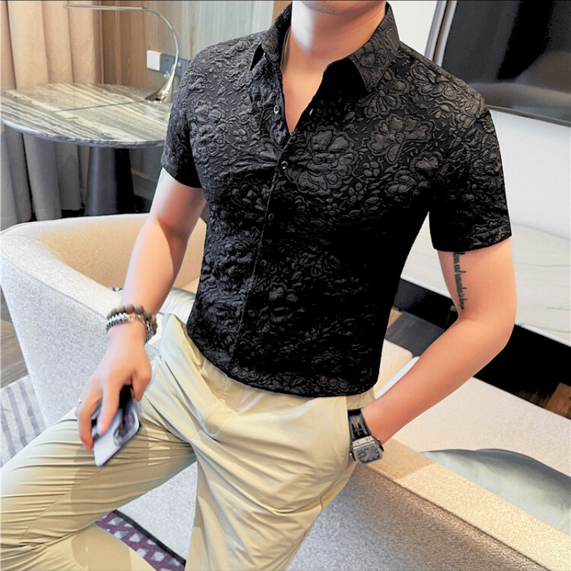 黒の花柄シャツを着て携帯を手に持つ男性のカジュアルスタイル