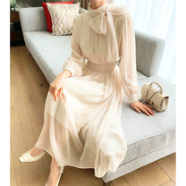 ボウタイ付きシフォンワンピースをソファに座って着用する女性