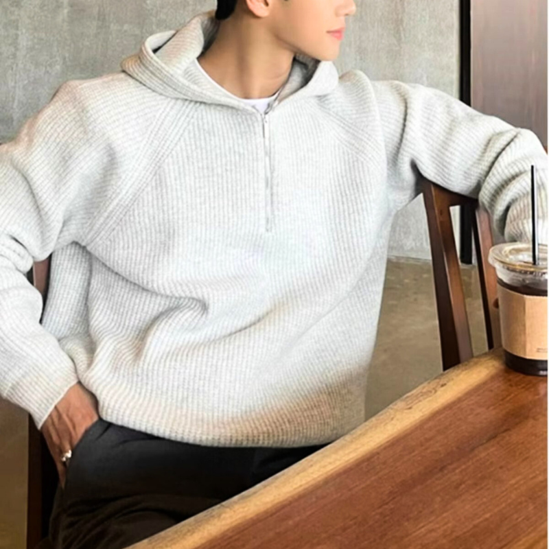 コーヒー片手にリラックスしたグレーニットコーデの男性
