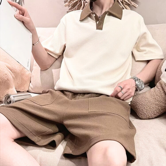 配色ポロシャツとブラウンハーフパンツを着た男性がソファでリラックスする夏の部屋着コーデ