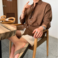カフェでの着席シーン。ハーフパンツとブラウンシャツの上品な夏スタイル