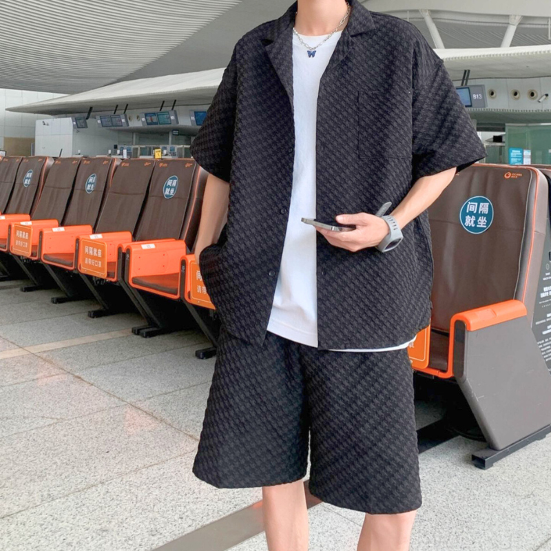 黒シャツセットアップを着た男性が空港待機エリアでスマホを持って立っている