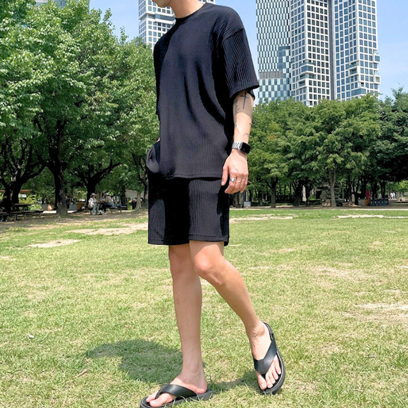 芝生の上で黒のプリーツセットアップをラフに着こなす男性