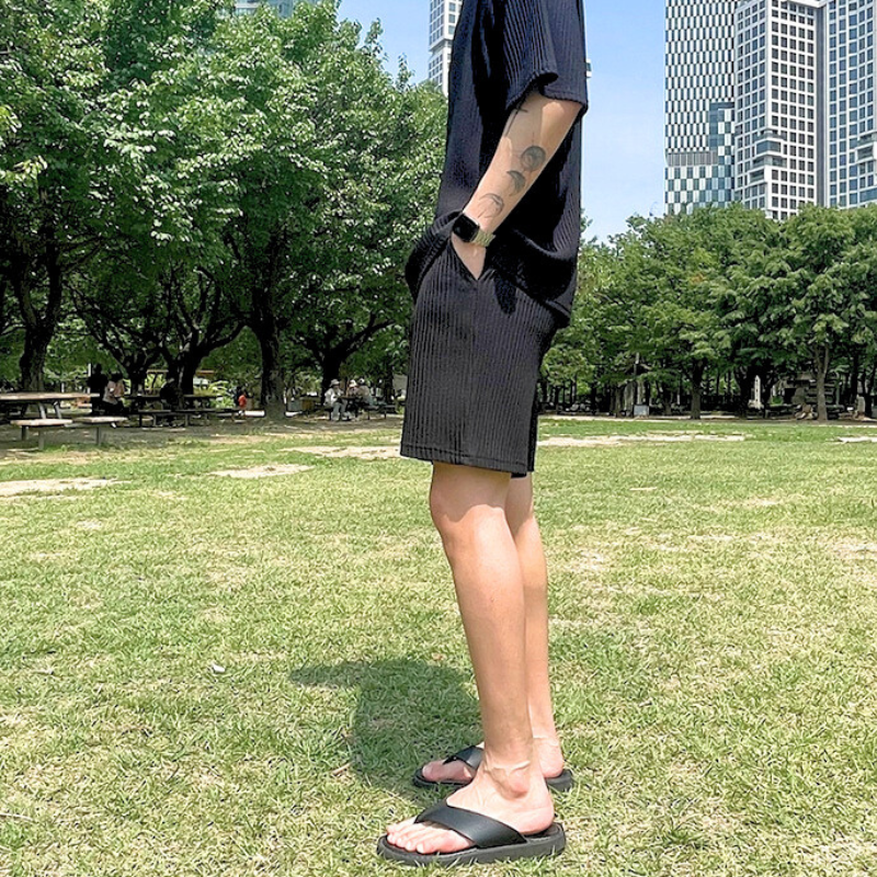 公園の芝生上でリラックスした姿勢の男性（黒ショートパンツセットアップ）