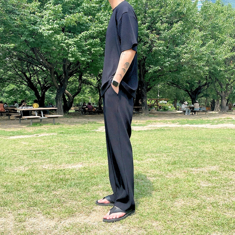 横向きで黒のセットアップを着用する男性（緑の芝生上）